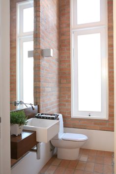 a white toilet sitting next to a window in a bathroom near a sink and mirror