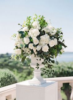 a white vase filled with flowers sitting on top of a wooden table next to a balcony