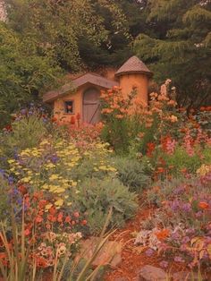 a garden filled with lots of flowers next to a small building in the middle of trees