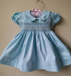 This beautiful dress is hand smocked with matching blue and hand embroidered with soft pink roses and green leaves on the bodice.  Dress is fully lined with soft cotton material. The back closes with a zip and tie sashes.  100% Cotton  Cold gentle machine wash Size 3-6 months (AU 00) Length 14.5" Chest circumference 19.5" Size 6-12 months (AU 0) Length 16" Chest circumference 20" Size 1 Length 18" Chest circumference 21" Size 2 Length 20" Chest circumference 22" Size 3 years  Length 22"  Chest c Blue Dress Baby, Pastel Blue Dress, Soft Pink Roses, Hand Embroidered Dress, Hand Smocked Dress, Girls Smocked Dresses, Baby Blue Dresses, Bleu Pastel, Hand Smock