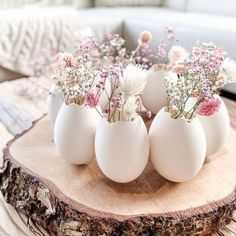 four eggs with flowers in them sitting on a wooden table next to a white couch