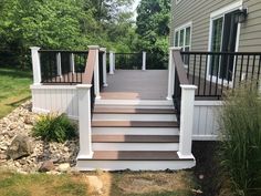 a deck with steps and railings leading to the front door, next to a house