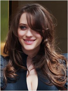 a woman with long brown hair smiling at the camera and wearing a black dress,