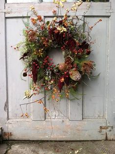 a wreath is hanging on the side of an old door with flowers and leaves around it