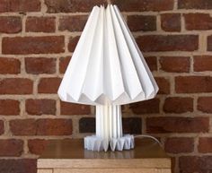 a white lamp sitting on top of a wooden table next to a brick wall and floor