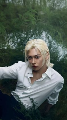 a woman with blonde hair and white shirt posing in front of green plants, looking at the camera