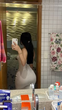 a woman taking a selfie in the bathroom mirror with her cell phone and other personal care products