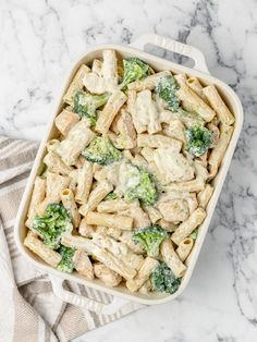 a casserole dish filled with pasta and broccoli on a marble surface