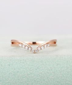 a rose gold wedding band with white diamonds on the top and bottom, in front of a light green background