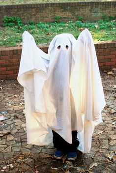 a person wearing a ghost costume standing in front of a brick wall and grass area