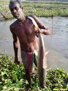 a man standing next to a body of water with a fish in it's mouth