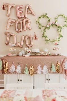 a table topped with pink and gold balloons next to a sign that says tea for two