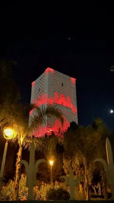 a tall building with red lights on it's side and palm trees in the foreground