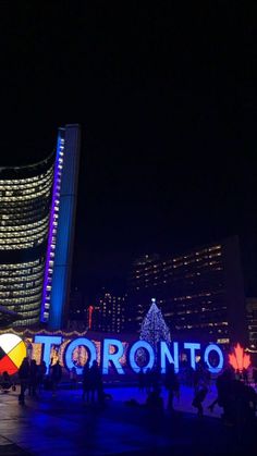 the toronto sign lit up at night with people standing around it and buildings in the background