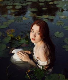 a woman is sitting in the water with lily pads on her chest and looking up