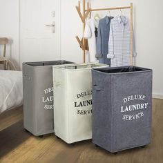 three laundry bins on the floor with clothes hanging from them and a bed in the background