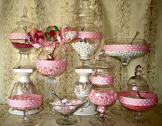 a table topped with lots of pink and white candies in vases next to each other