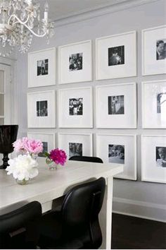 a white dining room table with black chairs and pictures on the wall behind it,