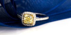 a fancy yellow diamond ring sitting on top of a blue cloth