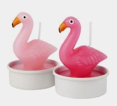 two pink flamingos sitting in small white containers with candles on each candle holders,