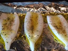 three fish fillets sitting on top of foil covered in seasoning and pepper sprinkles