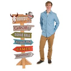 a man standing next to a wooden sign with arrows pointing in different directions and words