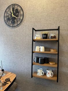 a clock mounted to the side of a wall next to a shelf filled with coffee cups