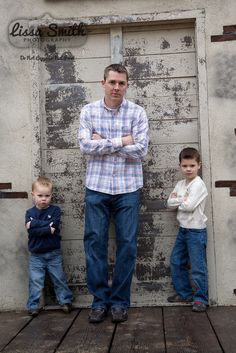 a man standing next to two small boys in front of a wooden door with his arms crossed