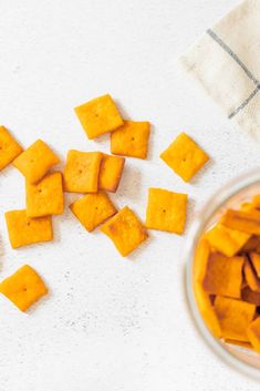 several pieces of cut up cheese next to a bowl of diced carrots on a white surface