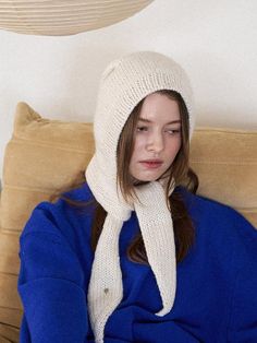 a woman sitting on a couch wearing a white knitted hat and scarf over her head