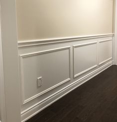 an empty room with white paneling and wood floors