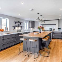 a large kitchen with wooden floors and gray cabinetry is pictured in this image, there are three stools at the center of the island