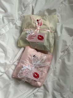 two wrapped presents sitting on top of a bed next to each other, tied with pink ribbon