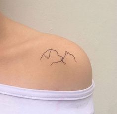 a woman's shoulder with a small tattoo of two cats on it, one cat is kissing the other