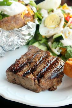 steak and salad on a white plate with foil wrapper next to the meat, as well as an egg