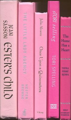 a row of pink books sitting on top of a book shelf next to each other