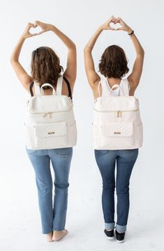 two women standing back to back with their hands in the air and one holding her purse