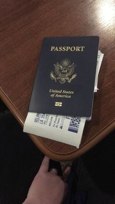 a person holding a passport sitting on top of a wooden table in front of a persons hand