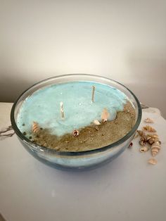 a bowl filled with sand and sea shells on top of a white tablecloth covered counter