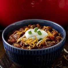 a blue bowl filled with chili and sour cream on top of a wooden cutting board