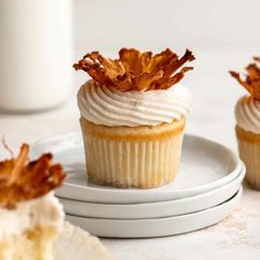 three cupcakes with white frosting and dried leaves on top sitting on plates