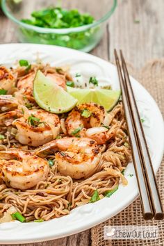 a white bowl filled with shrimp and noodles next to chopsticks on a table