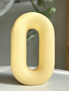 the letter o is made out of yellow plastic and sits on a table next to a potted plant