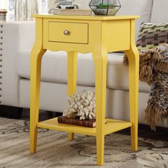 a yellow end table sitting on top of a rug next to a white couch in a living room