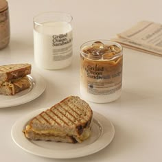 two plates with sandwiches on them next to a glass of milk and a jar of peanut butter