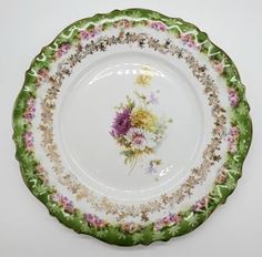 a green and white plate with flowers painted on the side, against a white background