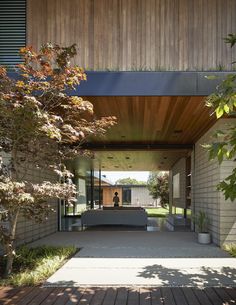 an entrance to a modern house with wood and concrete walls, surrounded by greenery