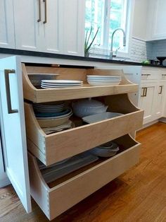 an open drawer in the middle of a kitchen with plates and bowls on it's bottom shelf