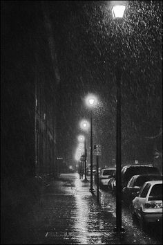 black and white photo of cars parked on the side of a street in the rain