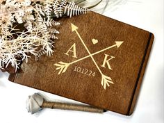 a personalized wooden guest book with an arrow and initials on it next to flowers